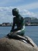 slávna socha Malej morskej víly v Kodani, v pozadí priemyselná časť mesta